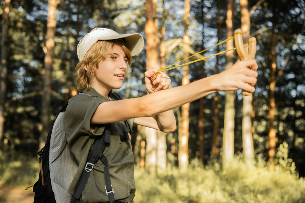A teenager enjoys an outdoor adventure playing in the forest with a slingshot.